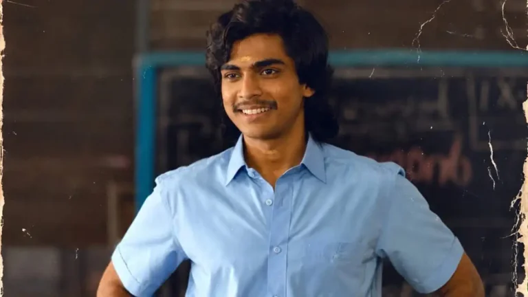 Smiling young man with dark wavy hair and a mustache wearing a light blue shirt in a classroom
